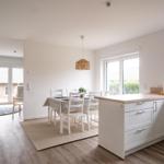 Küche mit Essbereich, weiße Schränke, Holzoberfläche und Fenster.