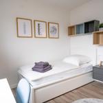 Schlafzimmer mit Bett, Nachttisch und Wandregalen. An der Wand hängen drei Bilder.