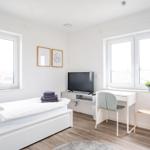 Schlafzimmer mit Bett, Fernseher, Schreibtisch und Fenstern.