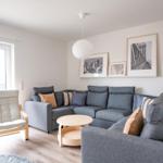 Wohnzimmer mit grauem Sofa, Holzstuhl und runden Tisch.