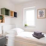 Schlafzimmer mit Bett, Nachttisch und Wandregalen. Fenster mit Pflanze und Bild.