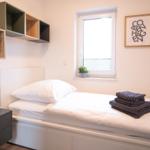 Schlafzimmer mit Bett, Nachttisch und Wandregal. Fenster und Bilder an der Wand.