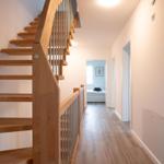 Holztreppe mit Metallgeländer führt zu einem Flur mit Holzboden und Türen zu Räumen.