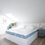 Schlafzimmer mit Dachschrägen, Doppelbett, Nachttisch und Stehlampe.