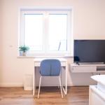 Schlafzimmer mit Schreibtisch, TV und Fenster. Bett mit Handtüchern. Holzboden und weiße Wände.