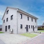 Modernes zweistöckiges Haus mit Steinmauer, Fenstern und Eingängen. Vorgarten mit Rasen und gepflastertem Weg.