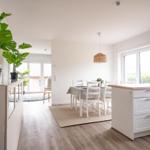 Küche mit Essbereich, weiße Möbel, Holzboden und große Fenster.