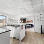 Küche mit Essbereich und Wohnzimmer im Hintergrund. Große Fenster und moderne Einrichtung.