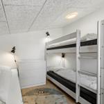 Zimmer mit Doppelstockbett und Einzelbett. Weiße Wände, Holzboden und Deckenleuchte.