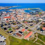 Aerial view of a coastal town with harbor, houses, and wind turbines in the distance.