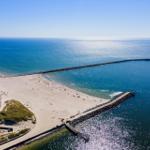 Aerial view of a beach with a long breakwater extending into the sea.