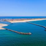 Aerielansicht von Hafen, Strand und Küstenlinie mit Steilufer und Windkraftanlage.