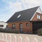Moderne Ein-Familienhaus mit rotem Backstein, schwarzem Dach und Holzgarage.