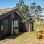 Holzhaus mit Grasdach, Terrasse und Gartenmöbel in natürlicher Umgebung.