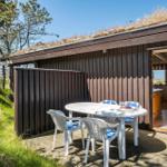 Hütte mit Grasdach und Terrasse mit Tisch und Stühlen. Küche sichtbar durch offene Tür.