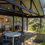 Terrasse mit Tisch und Stühlen, Blick in Wohnbereich, umgeben von Grünflächen.