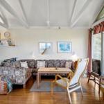 Wohnzimmer mit Sofa, Stuhl und TV. Große Fenster und Holzboden.