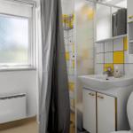 Badezimmer mit Dusche, Waschbecken und Toilette. Gelbe Fliesen und graue Vorhänge.