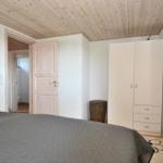 Schlafzimmer mit Bett, Kleiderschrank und Spiegel. Holzdecke und Tür sichtbar.