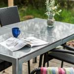 Außentisch mit Stühlen, Tasse, Zeitschrift und Blumenarrangement.