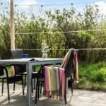 Terrasse mit Tisch, vier Stühlen und Decke. Hintergrund: Grünflächen und Bäume.