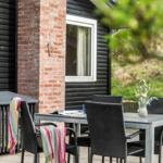 Terrasse mit Tisch und Stühlen, roter Ziegelsockel, grüne Vegetation im Hintergrund.