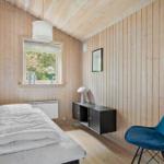 Schlafzimmer mit Holzwand, Bett, blauer Sessel und Fenster mit Blick auf Garten.