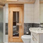 Bad mit Dusche, WC und Waschbecken. Holztür führt in die Badewanne.