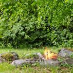 Feuerplatz im Grünen mit Steinring und Bäumen im Hintergrund.