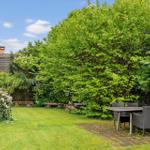 Garten mit Sitzgruppe, Bäumen und Grasfläche. Hintergrund: Haus mit Schieferdach.