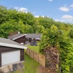 Haus mit Garage und Garten, umgeben von Bäumen unter blauem Himmel.