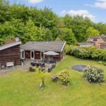 Holzhaus mit Terrasse, Garten und Trampolin. Umgeben von Bäumen und Grün.