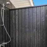 Außen-Dusche mit Duschbrause an schwarzer Holzwand und Meeresmuschel-Dekoration.