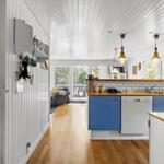Küche mit blauen Schränken und Holzoberfläche. Im Hintergrund Wohnbereich mit Sofa und Balkon.