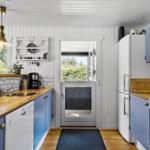 Küche mit blauen Schränken, Holzoberflächen und weißer Kachelwand. Tür führt nach draußen.