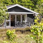Holzterrasse mit Tisch und Stühlen vor einem Haus mit großem Fensterbereich.