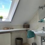 Badezimmer mit Dachschrägen, Waschbecken, Dusche und Fenster.