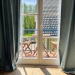 Durch die Glastüren ist ein Balkon mit Holztischen und Stühlen zu sehen.