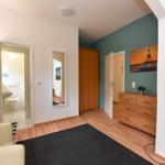 Zimmer mit Holzboden, Schrank, Schminktisch und Bad im Hintergrund.