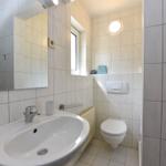 Badezimmer mit Dusche, Waschbecken und WC. Weiße Fliesen und Fenster.