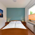 Schlafzimmer mit Doppelbett, Nachttischen und Fenster. Wandbild und Fernseher an der Wand.