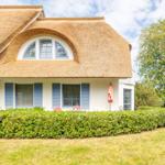 Haus mit Strohdach, blauen Fensterläden und grüner Hecke.