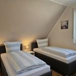 Zwei Einzelbetten mit Streifenbetten, Nachttische und ein Fenster mit Blick auf Bäume.