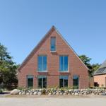 Moderne rote Backsteinhaus mit großen Fenstern und Steinmauer im Vordergrund.