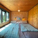 Schlafzimmer mit Doppelbett, Holzwand und großem Fenster zur Natur.