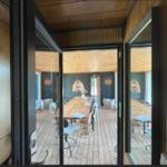 Durchgehende Glasfront führt in Esszimmer mit Holztisch und Stühlen.