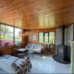 Wohnzimmer mit Holzdecke, Sofa, Kamin und großen Fenstern.