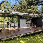 Schwarze Holzhütte mit Terrasse und Garten. Tisch und Stühle auf der Veranda.