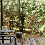 Terrasse mit Tisch, Stühlen und Hängesitz vor grüner Hecke.