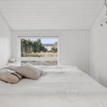 Bedroom with white wall paneling, bed, and view of green areas through window.